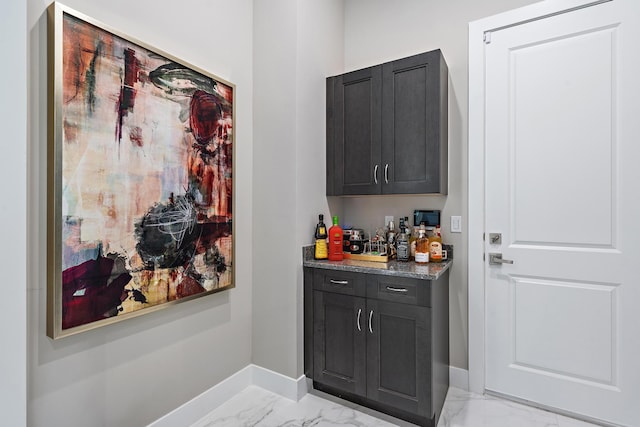 bar with marble finish floor, a bar, and baseboards