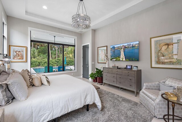 bedroom with a chandelier, light wood-type flooring, and a raised ceiling