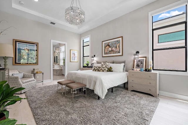 bedroom with an inviting chandelier, ensuite bathroom, light wood-type flooring, and a tray ceiling