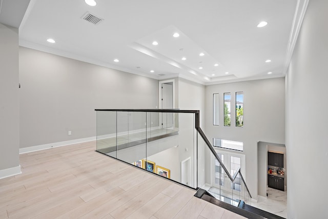 hall with light wood-type flooring, a tray ceiling, and ornamental molding