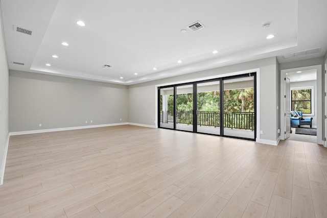 spare room with light hardwood / wood-style floors, a tray ceiling, and a healthy amount of sunlight