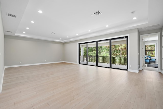 spare room with a tray ceiling, visible vents, and light wood-style floors