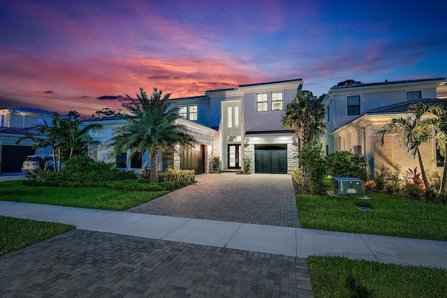 view of front of property with stucco siding, a lawn, decorative driveway, stone siding, and an attached garage