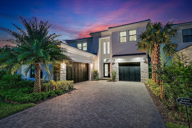 contemporary home featuring stone siding, stucco siding, decorative driveway, and a garage