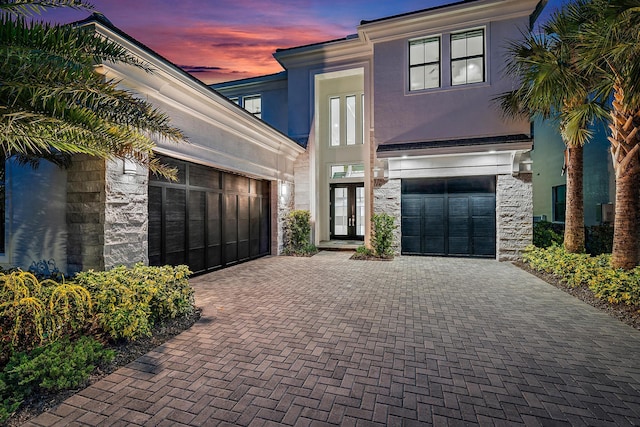 modern home featuring stone siding, stucco siding, decorative driveway, and a garage