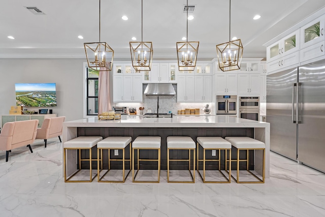 kitchen with appliances with stainless steel finishes, white cabinets, hanging light fixtures, backsplash, and a large island with sink