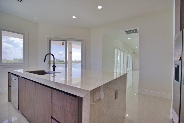 kitchen featuring a water view, sink, light stone countertops, a center island with sink, and light tile patterned floors