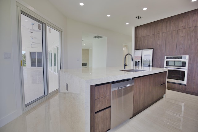 kitchen featuring an island with sink, sink, light stone counters, appliances with stainless steel finishes, and light tile patterned floors