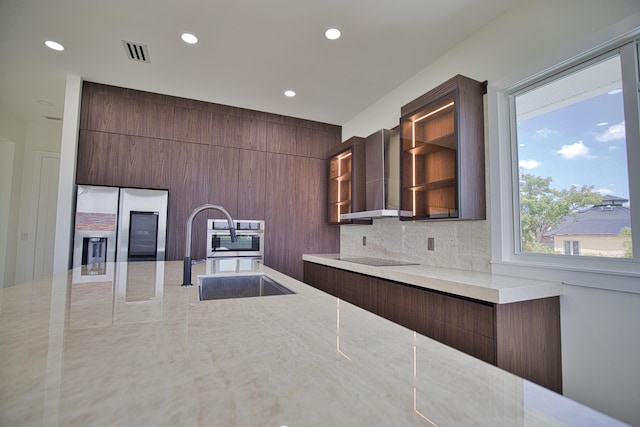 kitchen featuring tasteful backsplash, wall chimney range hood, stainless steel refrigerator with ice dispenser, sink, and light stone countertops