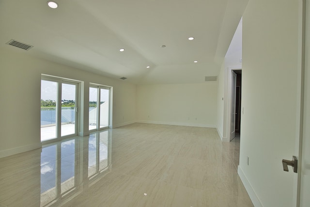 tiled empty room featuring a water view and vaulted ceiling