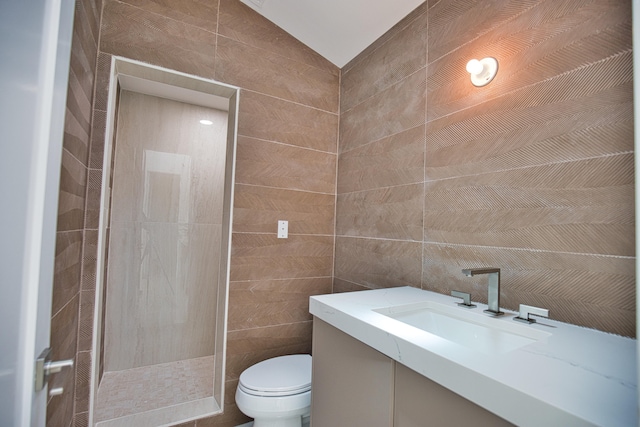 bathroom with vanity, a tile shower, toilet, and tile walls