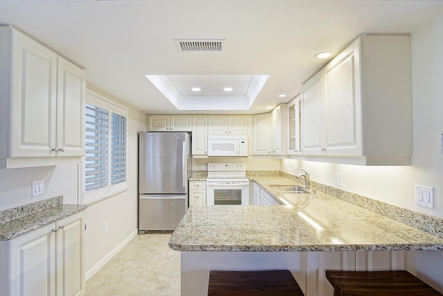 kitchen with kitchen peninsula, white appliances, a raised ceiling, sink, and white cabinetry