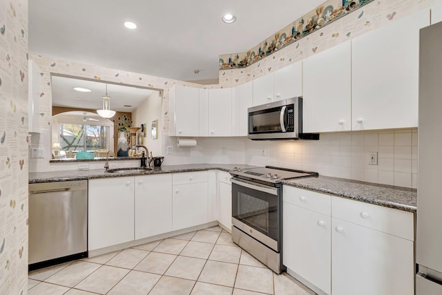kitchen with a sink, backsplash, appliances with stainless steel finishes, white cabinets, and light tile patterned floors