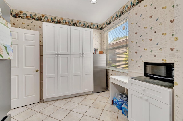 kitchen with light tile patterned floors, white cabinets, freestanding refrigerator, and black microwave