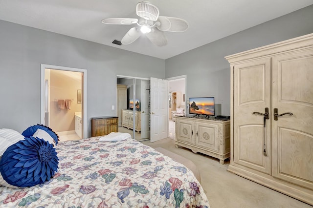 bedroom featuring ensuite bath, light colored carpet, multiple closets, and ceiling fan