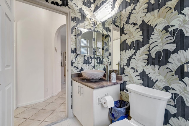 bathroom with wallpapered walls, baseboards, toilet, tile patterned floors, and vanity