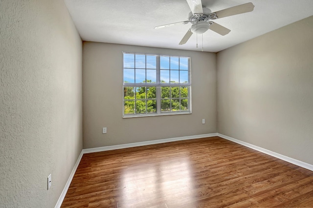 empty room featuring a ceiling fan, baseboards, wood finished floors, and a textured wall