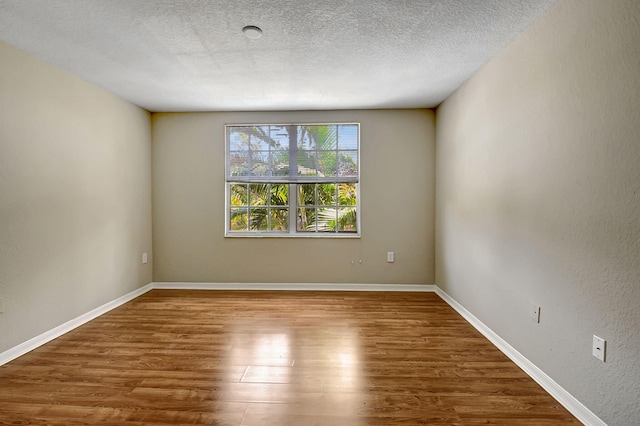 empty room with a textured ceiling, baseboards, and wood finished floors