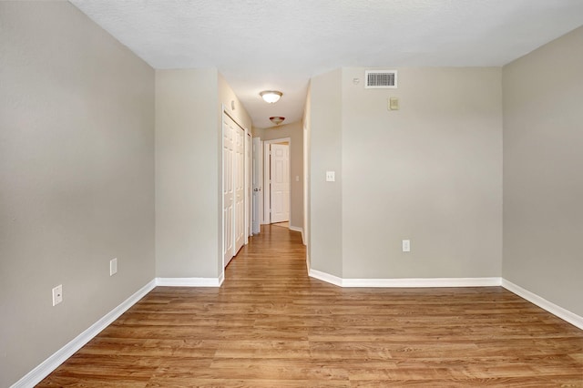 corridor with light wood-style floors, visible vents, a textured ceiling, and baseboards