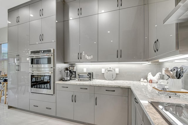 kitchen featuring stainless steel double oven, light stone countertops, and backsplash