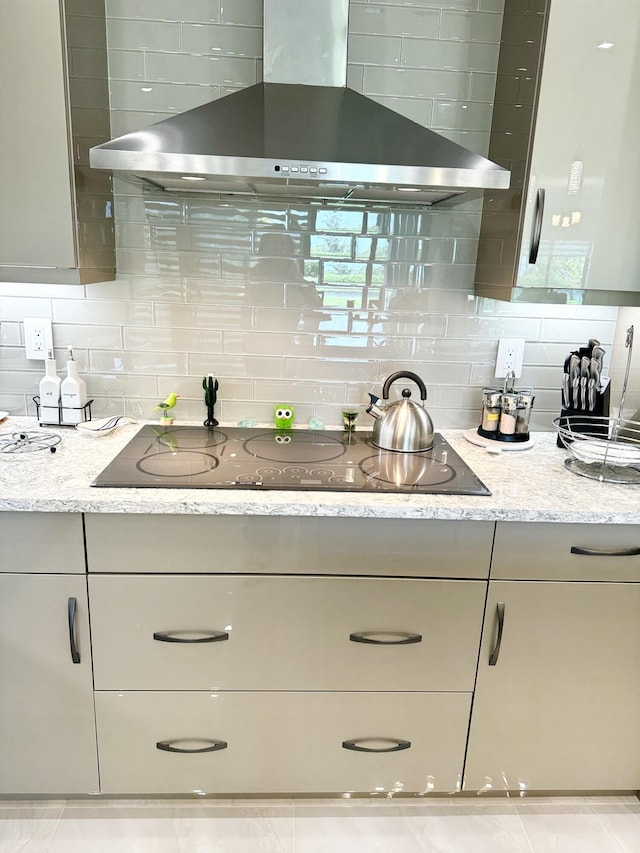 kitchen with light stone counters, wall chimney range hood, decorative backsplash, and black electric stovetop