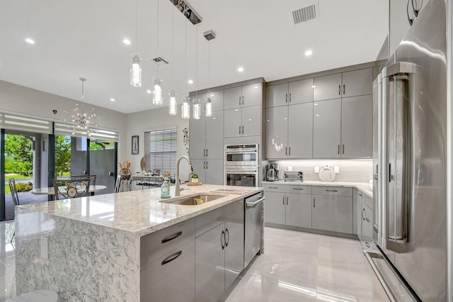 kitchen with sink, hanging light fixtures, gray cabinets, an island with sink, and stainless steel appliances