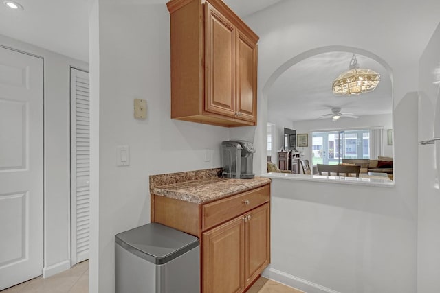 kitchen with arched walkways, brown cabinets, light tile patterned floors, recessed lighting, and ceiling fan