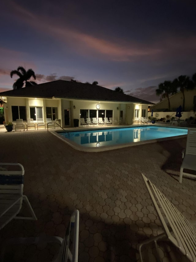 pool at dusk featuring a patio area and a community pool