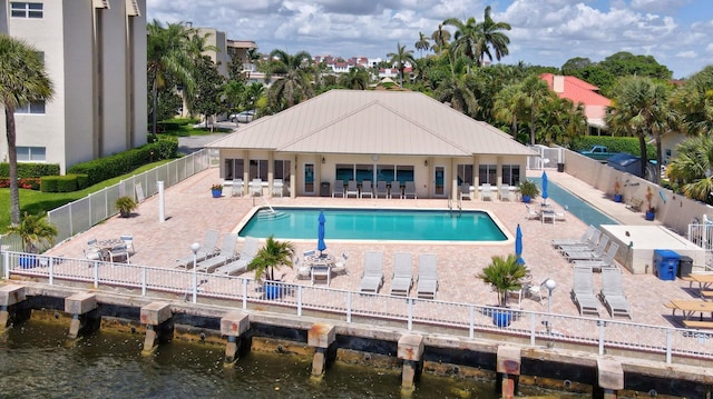 community pool with a water view, a patio area, and fence