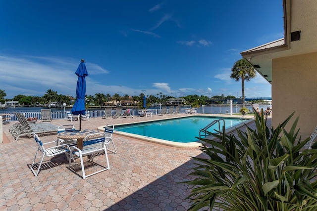 community pool with a water view, fence, and a patio