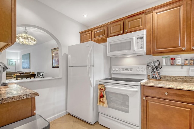 kitchen featuring white appliances, light tile patterned floors, baseboards, arched walkways, and brown cabinetry