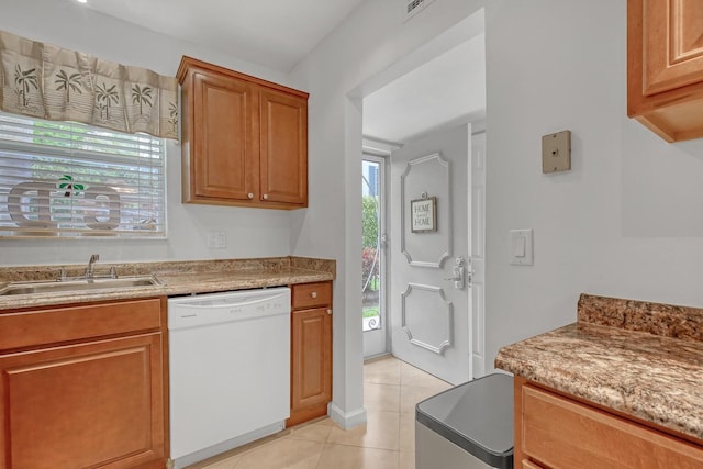 kitchen with brown cabinets, light tile patterned floors, a sink, light stone countertops, and dishwasher