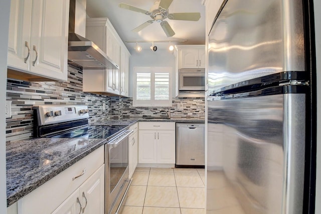 kitchen featuring wall chimney range hood, appliances with stainless steel finishes, white cabinetry, tasteful backsplash, and light tile patterned flooring