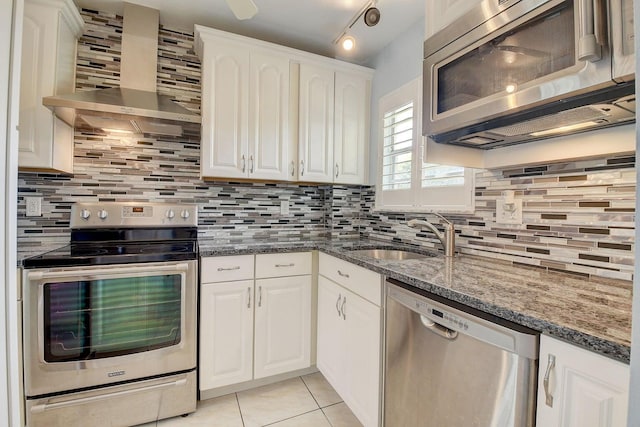 kitchen with sink, white cabinetry, dark stone countertops, appliances with stainless steel finishes, and wall chimney range hood