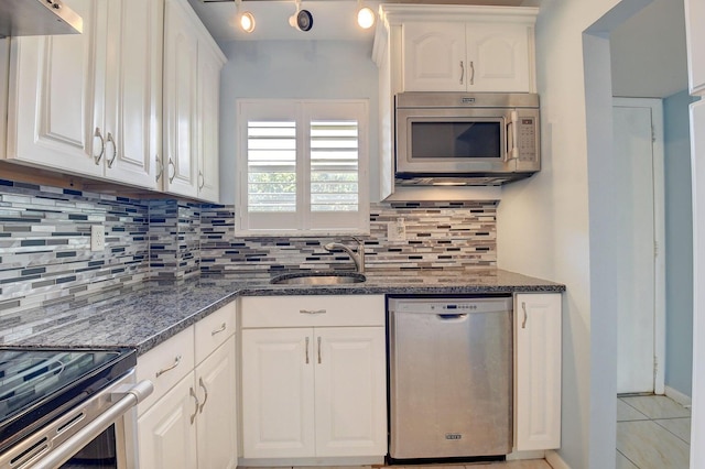 kitchen with appliances with stainless steel finishes, white cabinetry, sink, dark stone counters, and decorative backsplash