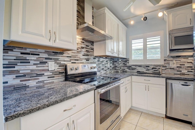 kitchen with sink, appliances with stainless steel finishes, dark stone countertops, white cabinets, and wall chimney exhaust hood