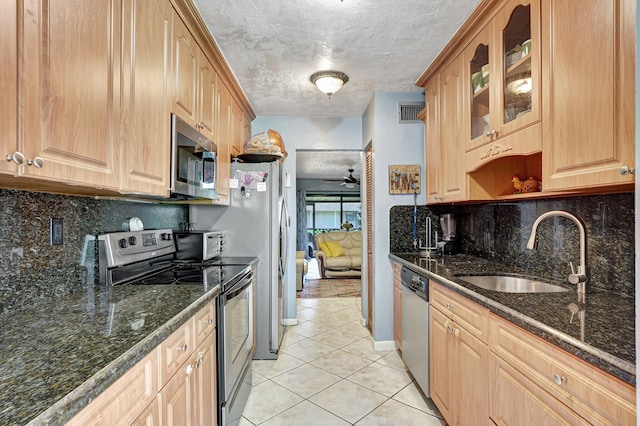 kitchen featuring ceiling fan, stainless steel appliances, dark stone counters, and sink