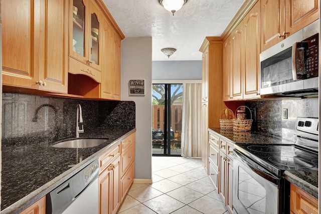 kitchen with appliances with stainless steel finishes, light tile patterned floors, sink, and dark stone counters