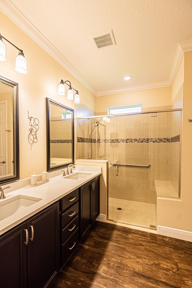 bathroom with ornamental molding, hardwood / wood-style floors, double sink vanity, and a shower with shower door