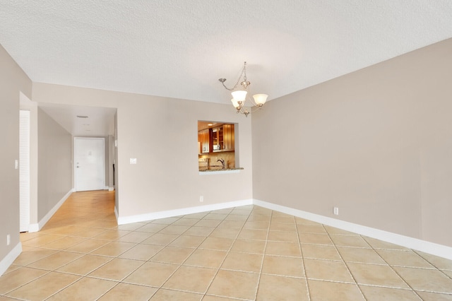 empty room featuring light tile patterned floors, sink, a chandelier, and a textured ceiling