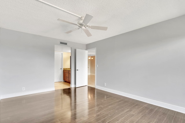 unfurnished bedroom featuring ensuite bath, a textured ceiling, ceiling fan, and hardwood / wood-style floors