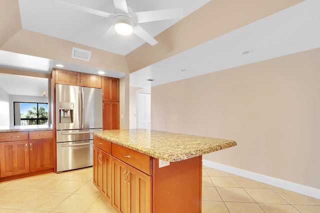 kitchen with ceiling fan, light stone countertops, a kitchen island, stainless steel fridge, and light tile patterned floors