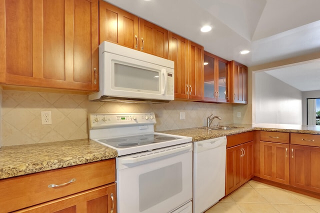 kitchen with light tile patterned flooring, white appliances, sink, light stone countertops, and backsplash