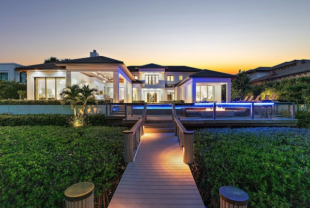 back house at dusk featuring a pool side deck