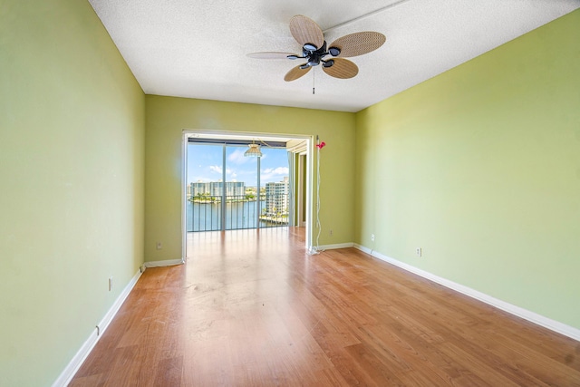 empty room featuring ceiling fan, light hardwood / wood-style flooring, a water view, and a textured ceiling