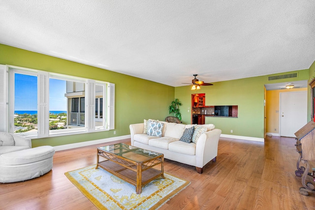 living room featuring ceiling fan, a textured ceiling, and light hardwood / wood-style flooring