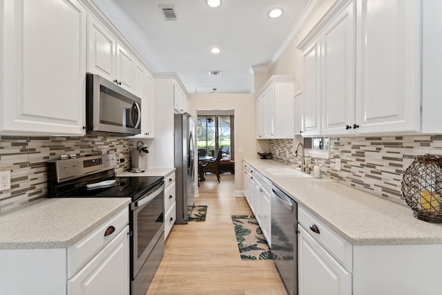 kitchen with light hardwood / wood-style flooring, appliances with stainless steel finishes, crown molding, sink, and white cabinets