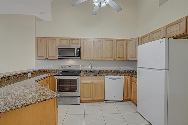 kitchen with sink, appliances with stainless steel finishes, a towering ceiling, light tile patterned flooring, and dark stone counters