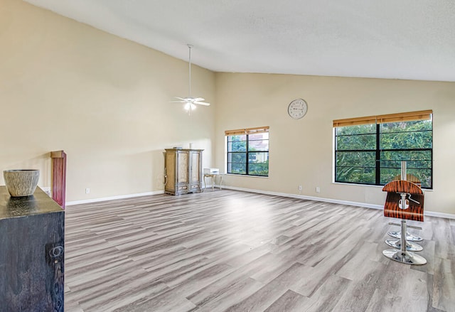 living room with vaulted ceiling, ceiling fan, a wealth of natural light, and light hardwood / wood-style flooring