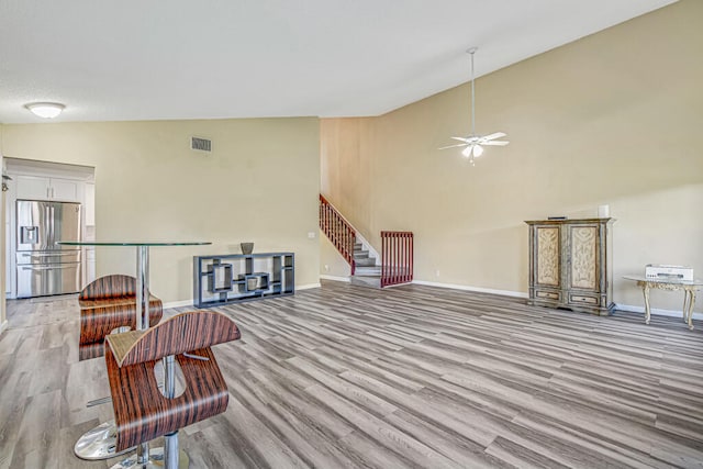 living room with ceiling fan, light hardwood / wood-style flooring, and vaulted ceiling